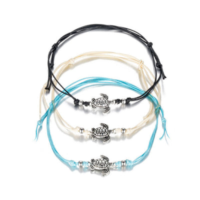 3 bracelets de cheville avec amulette tortue de mer en métal argenté et cordon bleu blanc ou noir sur sol blanc Kaosix