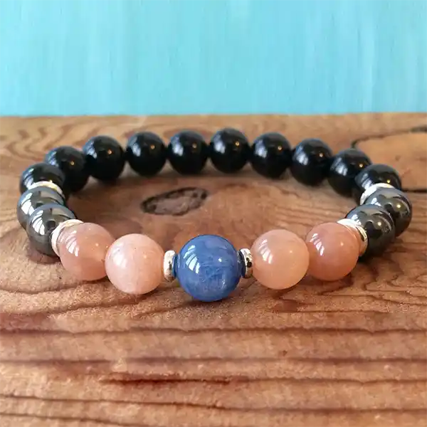 Bracelet Onyx Hématite Pierre de Soleil Cyanite sur un plancher en bois avec un fond bleu kaosix