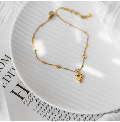 Bracelet de cheville en acier inoxydable doré pendentif cœur et zircons cubiques posé sur une assiette blanche Kaosix