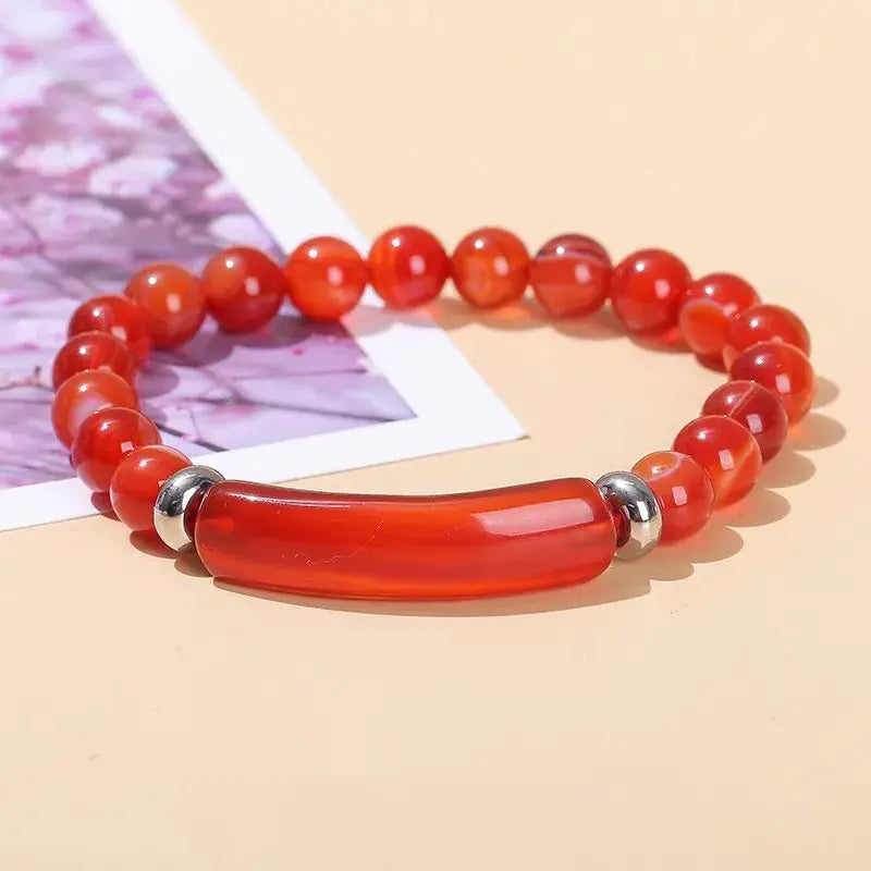 Bracelet en Agate Rouge Bande Courbe et Perles posé à plat à cheval sur une photo et un sol beige Kaosix