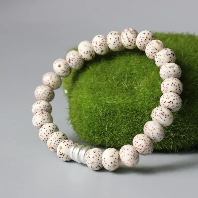 Bracelet tibétain graine de bodhi protection posé sur une grosse boule verte et sur un sol gris Kaosix