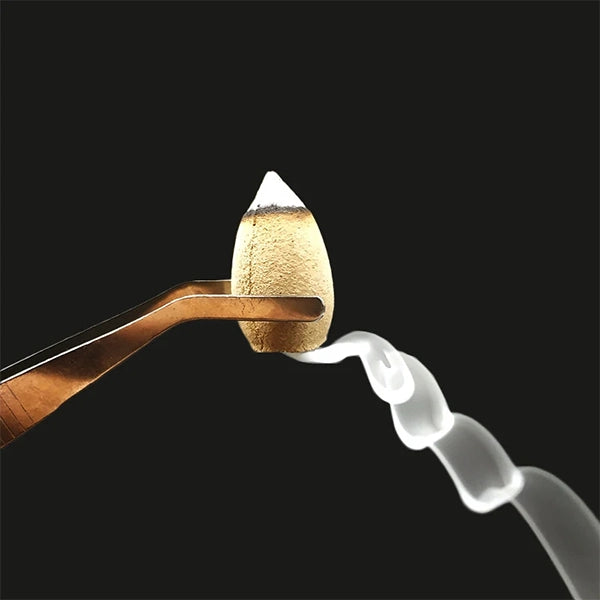 Cône d'Encens à Refoulement tenu par une pince sur fond noir kaosix