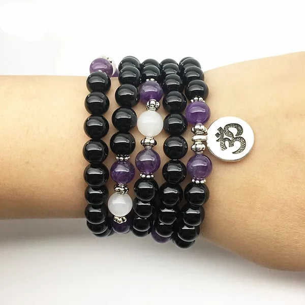 Mala 108 perles Onyx Noir Améthyste Om au poignet d'une femme et sur fond blanc kaosix