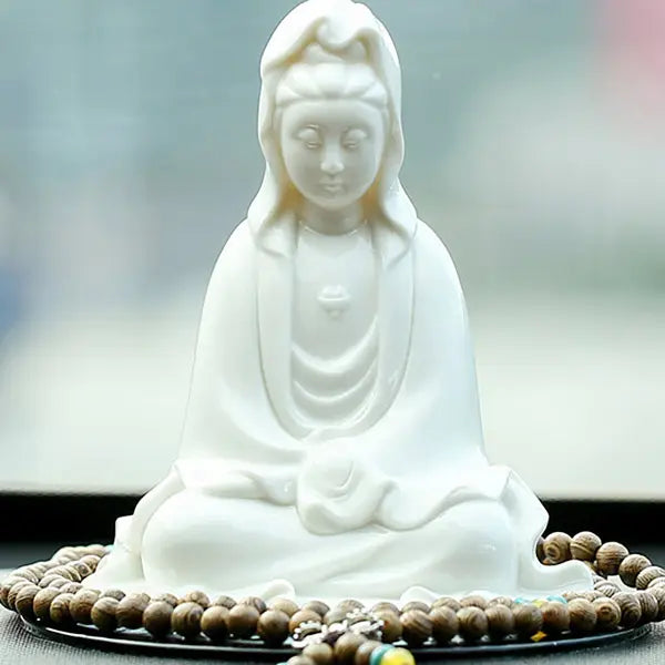 Statue Guanyin Déesse de la Compassion posé sur un sol gris avec un fond d'écran vert-gris flou Kaosix