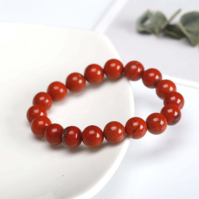 Bracelet Jaspe Rouge clarté posé à moitié sur une assiette blanche et à moitié sur une nappe de table Kaosix