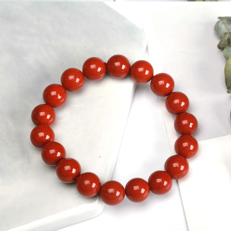 Bracelet Jaspe Rouge clarté posé à moitié sur une plaque de marbre blanche et à moitié sur une nappe de table Kaosix