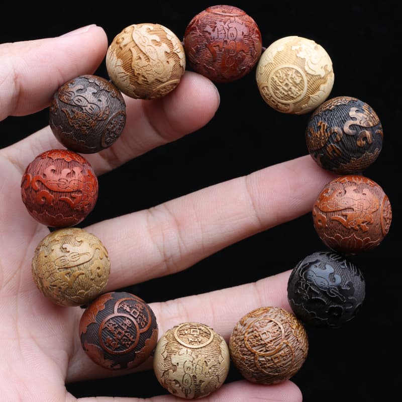 Bracelet fengshui PiXiu en perles de bois colorees entre les doigts d'une main Kaosix
