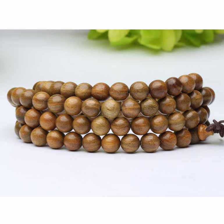 Bracelet mala tibétain bois santal 108 perles enroulé et posé sur un sol blanc avec une laitue verte en fond flou Kaosix