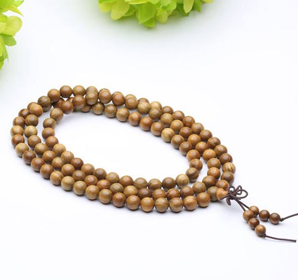 Bracelet mala tibétain bois santal 108 perles posé sur un sol blanc avec une laitue verte en fond Kaosix