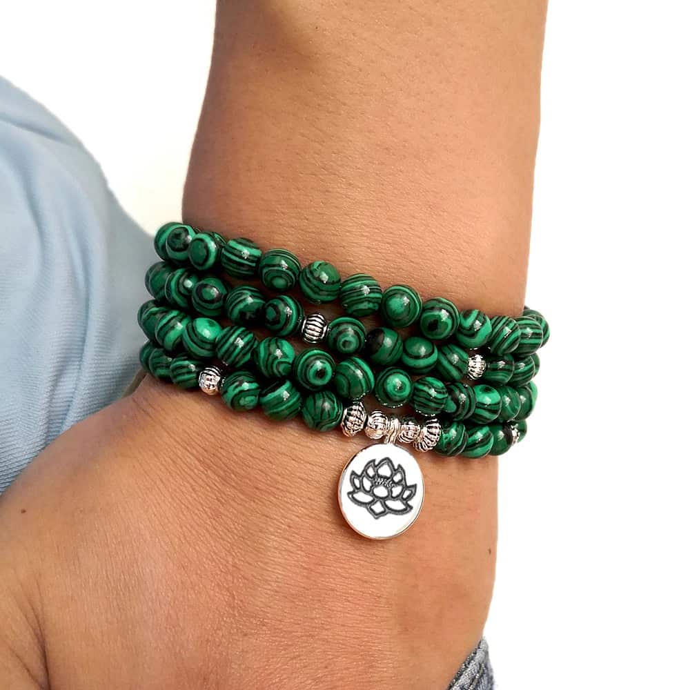 Mala 108 perles Malachite et symbole du Lotus (boule 6 mm) sur fond blanc avau poignet dun jeune homme vue en gros plan Kaosix