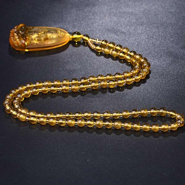 Pendentif Bouddha Bodhisattva en Citrine posé à plat sur un sol gris foncé Kaosix