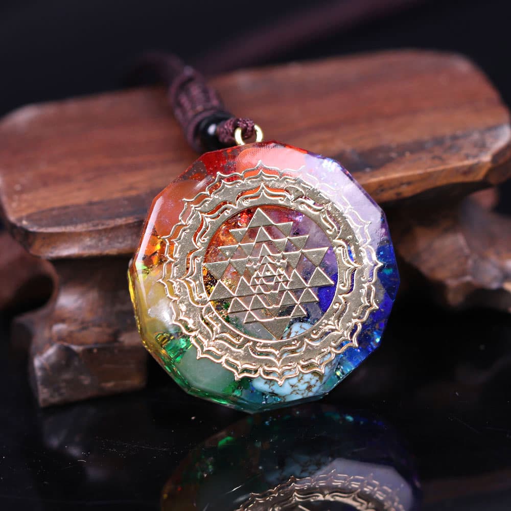 Pendentif Orgonite Sri Yantra 7 Chakras pose sur un socle en bois et fond noir Kaosix
