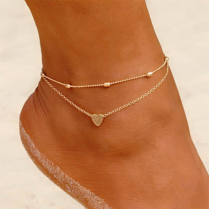 Set de deux bracelets de cheville avec amulette cœur couleur doré autour d'une cheville de femme Kaosix
