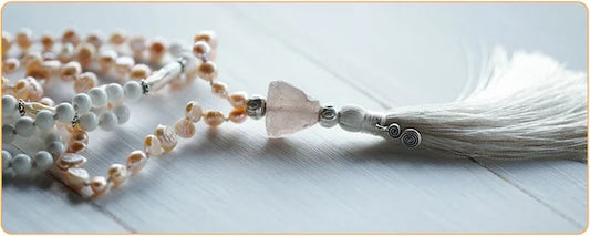 Bracelet collier mala avec perles blanches et pompon blanc posé sur une table en bois gris Kaosix