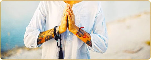 Une femme debout les mains jointes en train de prier et un mala autour de son poignet droit Kaosix