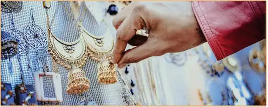 une main tenant une boucle d'oreille en or suspendue à un porte bijoux Kaosix