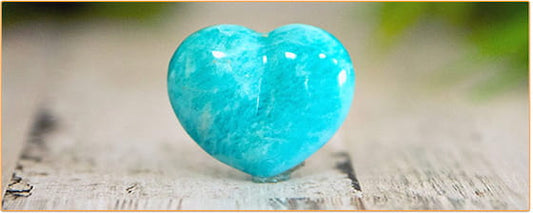 galet d'Amazonite en forme de cœur posé sur une table en bois avec un fond vert Kaosix