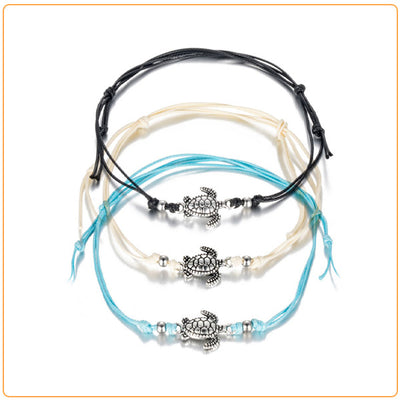 3 bracelets de cheville avec amulette tortue de mer en métal argenté et cordon bleu blanc ou noir sur sol blanc Kaosix