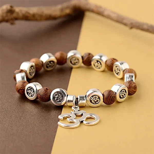 Bracelet OM Bois et Métal sur une surface jaune et marron avec une branche de bois en arrière plan kaosix