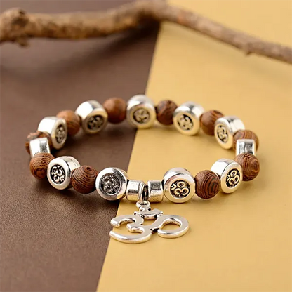 Bracelet OM Bois et Métal sur une surface jaune et marron avec une branche de bois en arrière plan kaosix