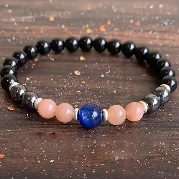 Bracelet Onyx Hématite Pierre de Soleil Cyanite sur un plancher en bois avec des paillettes kaosix