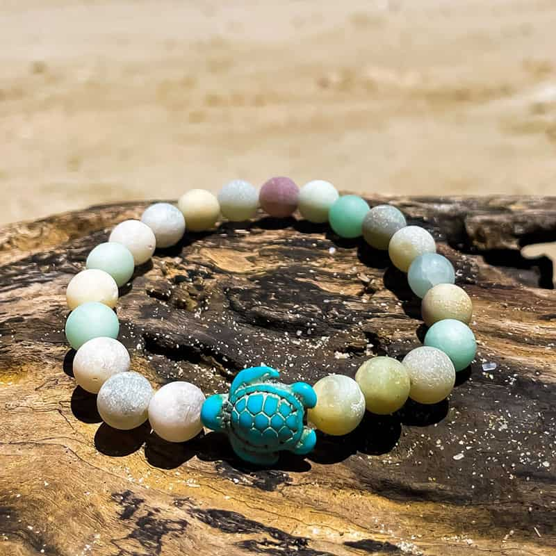 Bracelet Pierre d’Amazonite Tortue Marine posé sur un morceau de bois sur une plage Kaosix