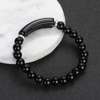 Bracelet en Agate Noire Bande Courbe et Perles posé sur un socle en marbre et un sol gris foncé Kaosix