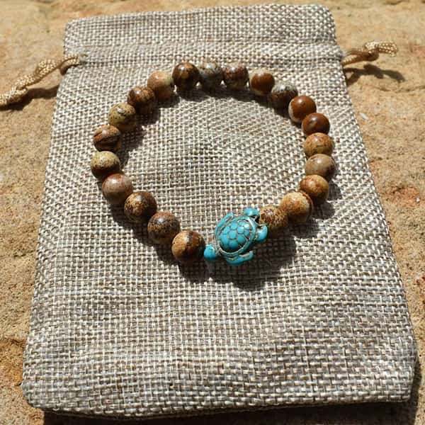 Bracelet jaspe brun Tortue Marine posé sur un sac en toile sur du sable au soleil Kaosix