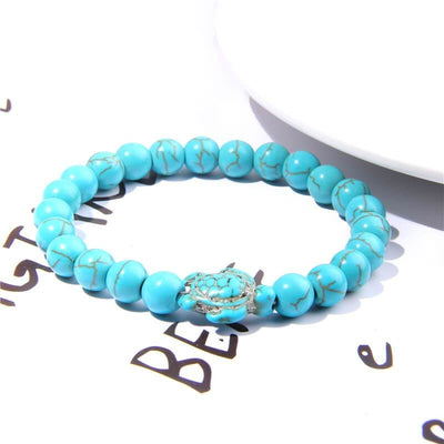Bracelet pierre bleu turquoise tortue marine posé sur une page blanche avec inscriptions à l'encre noire Kaosix