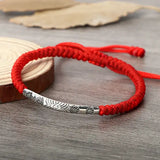 Bracelet tibétain rouge porte bonheur soleil sur un socle en bois posé sur une table en bois Kaosix