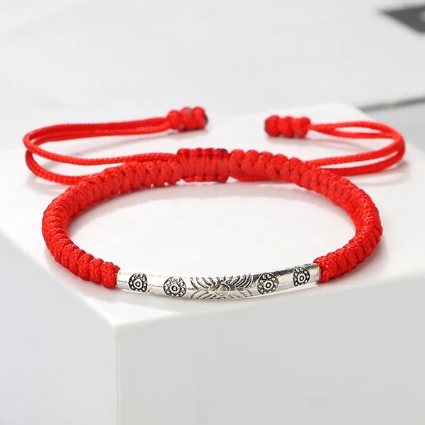 Bracelet tibétain rouge porte bonheur soleil sur un socle en plastique blanc Kaosix