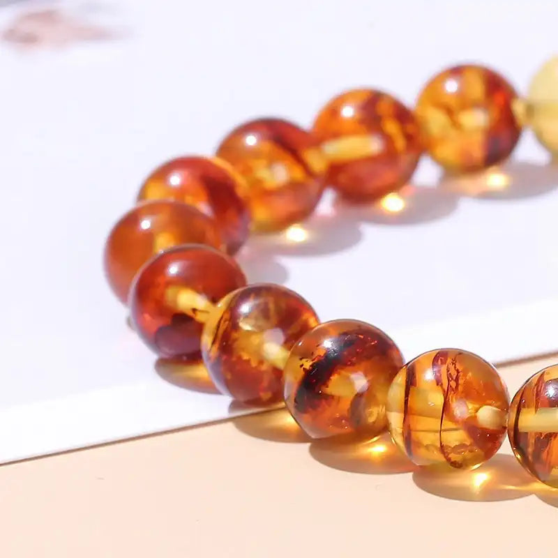 Gros plan sur les perles du Bracelet en Perles d’Ambre Jaune posé sur une table couleur saumon à coté d'une feuille blanche Kaosix