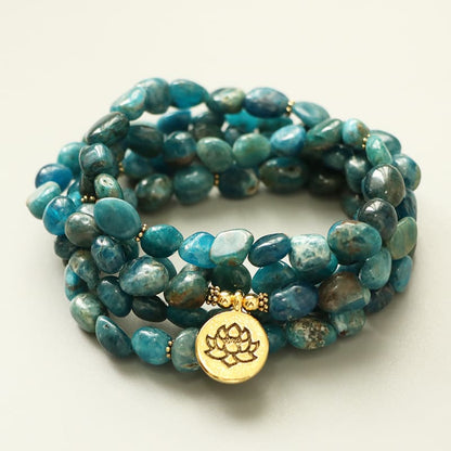 Mala 108 perles Apatite Bleue Symbole du Lotus posé sur un sol de couleur beige Kaosix