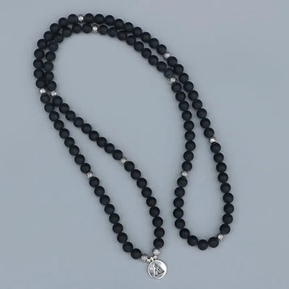 Mala 108 perles Onyx Noir Bouddha déroulé sur un sol gris kaosix