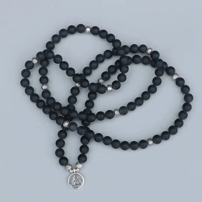 Mala 108 perles Onyx Noir Bouddha étalé sur un sol gris kaosix