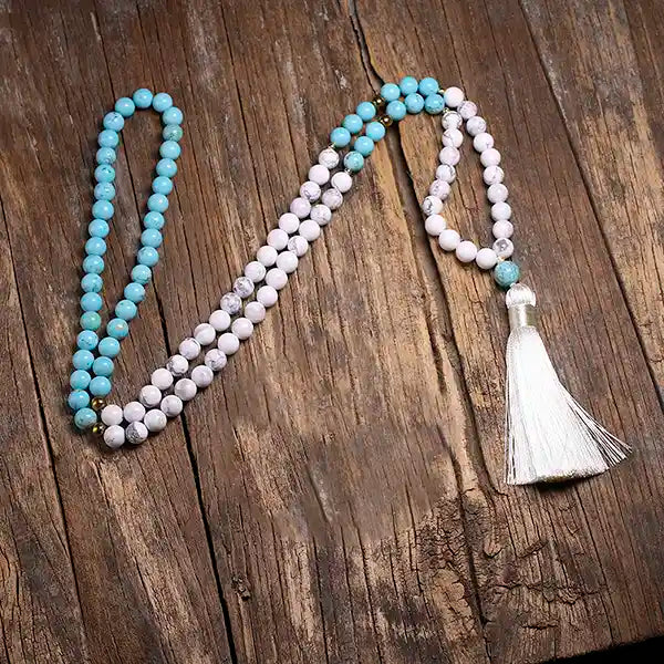 Mala 108 perles howlite blanche et turquoise Pompon déroulé sur un parquet en bois et vue de dessus Kaosix