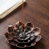 Porte Encens Fleur De Lotus Bronze posé sur une table en bois avec un bâton d'encens et un livre ouvert Kaosix