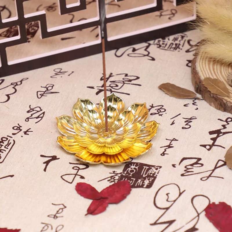 Porte Encens Fleur De Lotus Doré posé sur un tapis chinois et entouré de feuilles d'arbre Kaosix
