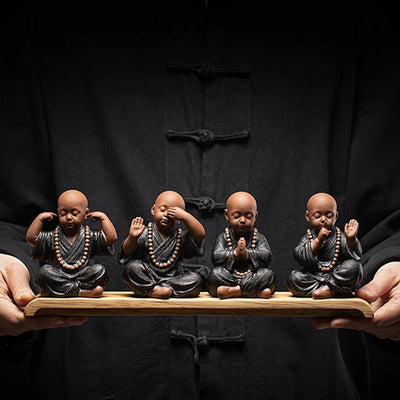 Quatre Statues de Moines Tibétains Compagnons de Sérénité sur un socle en bois tenu par un homme en tunique chinoise noire kaosix