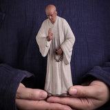Statue Moine Bouddhiste Humilité et Respect Debout Blanc posée sur les mains d'un homme vue en gros plan Kaosix