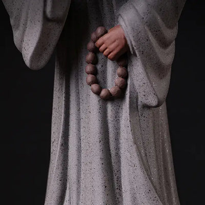 Statue Moine Bouddhiste Humilité et Respect Debout Blanc sur fond noir vue en gros plan de la main gauche tenant un mala de perles marron Kaosix