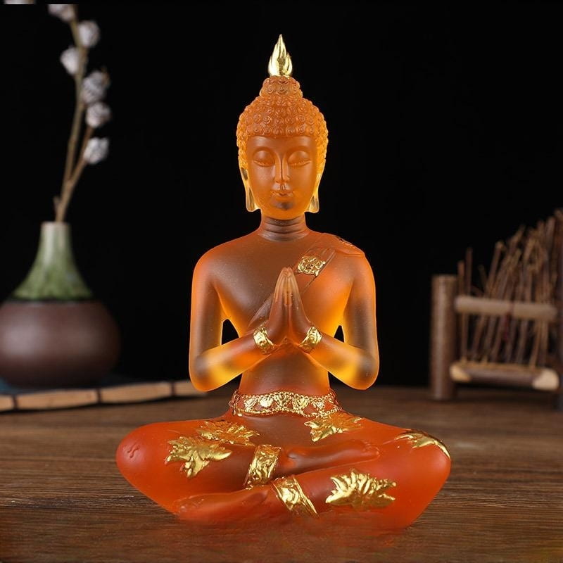 Statuette de Bouddha en résine translucide orange assis de face sur une table en bois et un fond noir Kaosix