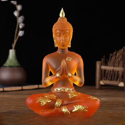 Statuette de Bouddha en résine translucide orange assis de face sur une table en bois et un fond noir Kaosix