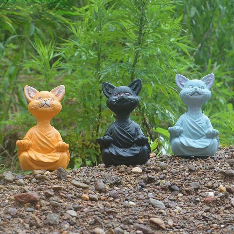 Trois statues Chat Bouddha Zen orange noir et gris assis dans la nature sur un tas de graviers Kaosix