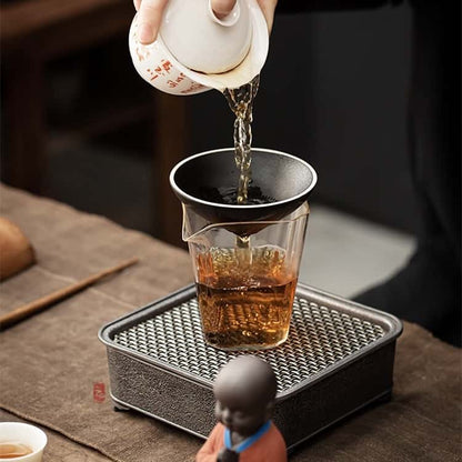 Une main qui verse du thé depuis une théière dans un verre avec la chapeau chinois qui sert de filtre pour le thé Kaosix