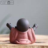 statuette bouddha rieur fortune robe orange vue de dos assis sur une table en bois kaosix