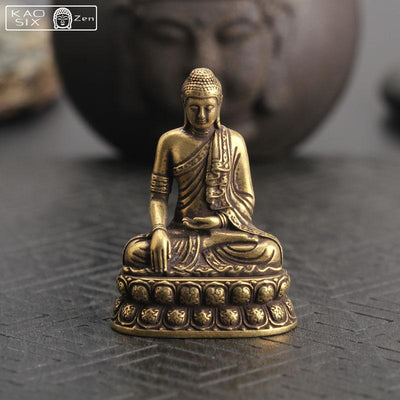 Statue Bouddha de la médecine de face posé sur une table avec une grosse tête de Bouddha en fond kaosix
