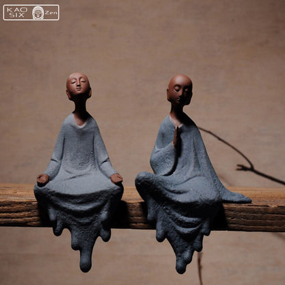 2 statues moine zen assis sur une planche en bois avec un arrière-plan marron  kaosix