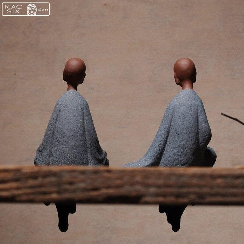 2 statues moine zen assis sur une planche en bois avec un arrière-plan marron et vue de dos kaosix