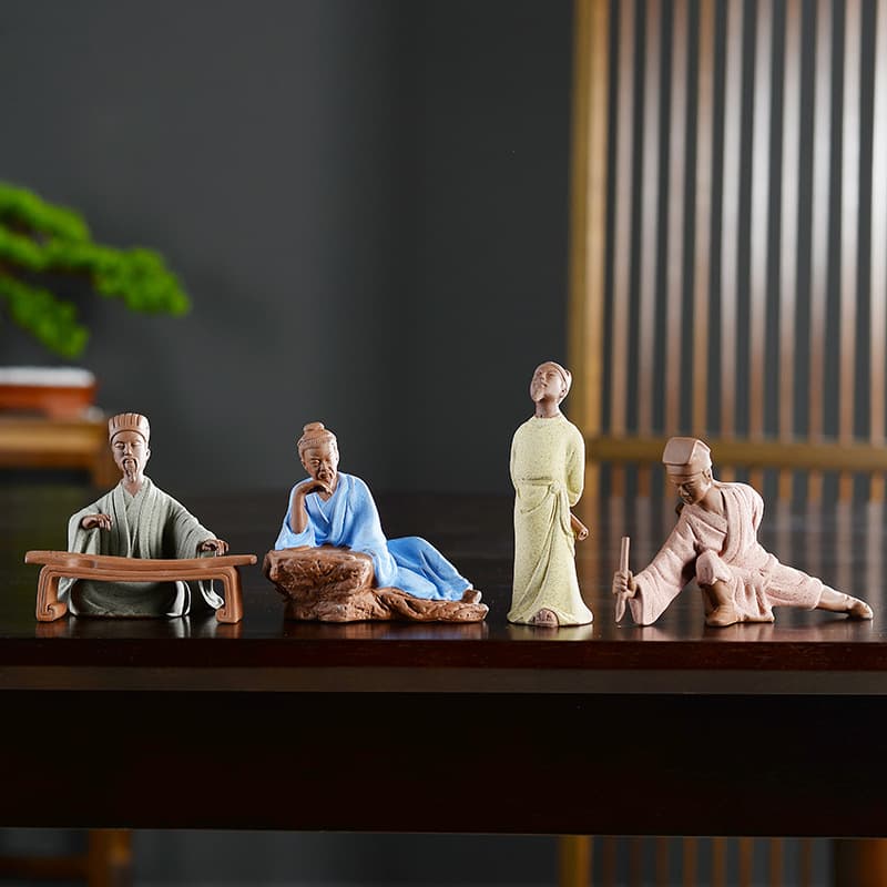 4 statues chinoises personnages historiques Zhuge Liang Lu Yu Li Bai Tang Yin posées sur une table en bois laqué sombre avec un fond flou Kaosix